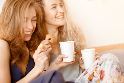 Two sisters laughing, drinking coffee, and eating Thanksgiving breakfast in bed. 
