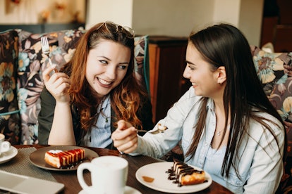 Two amazing caucasian woman sitting in a coffee shop smiling having fun while eating a cake and drin...