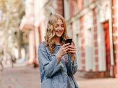 portrait of a young cute blonde with curly hair looking at iPhone and smiling