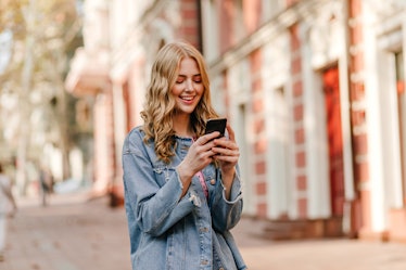 portrait of a young cute blonde with curly hair looking at iPhone and smiling