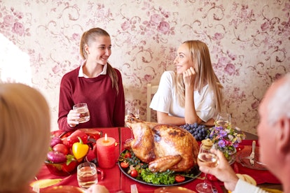 Two blonde sisters laugh and talk while they sit at a Thanksgiving dinner table.