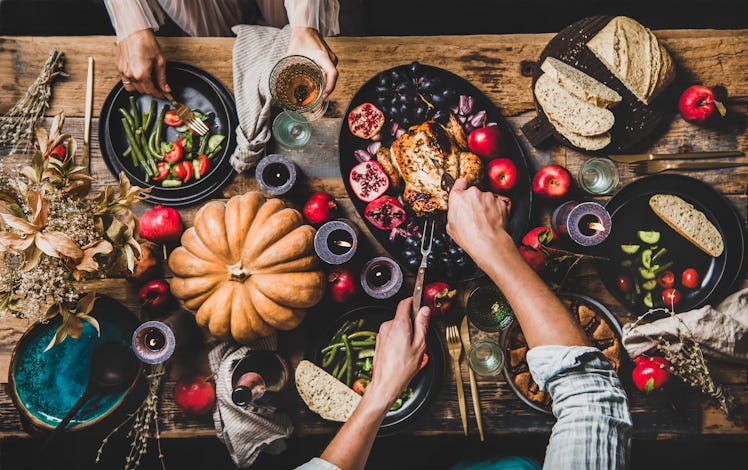 A couple dishes out food onto their plates from a colorful and festive Thanksgiving spread.