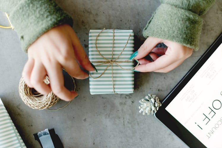 A woman ties a string bow on an engagement gift for her friend wrapped in green and white striped pa...