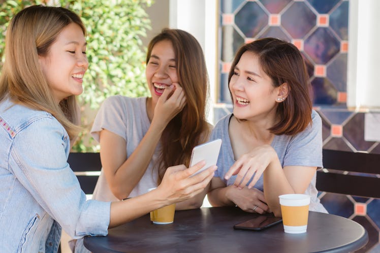 Cheerful asian young women sitting in cafe drinking coffee with friends and talking together. Attrac...