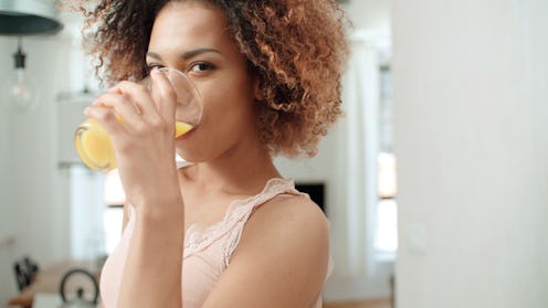 Happy mixed race woman holding orange juice and looking to camera.