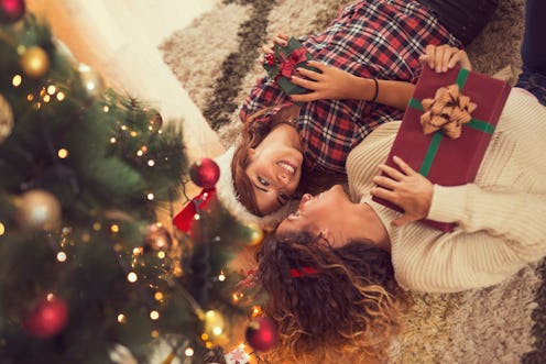 High angle view of two beautiful women lying on a carpet on a living room floor, holding nicely wrap...