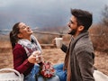 A couple laughs during a Thanksgiving picnic in autumn.