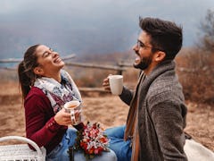 A couple laughs during a Thanksgiving picnic in autumn.