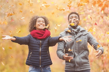 Happy afro couple throwing autumn fall leaves, walking and having fun in park