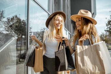 Two happy girlfriends looking on the shopwindow while standing with shopping bags near the mall