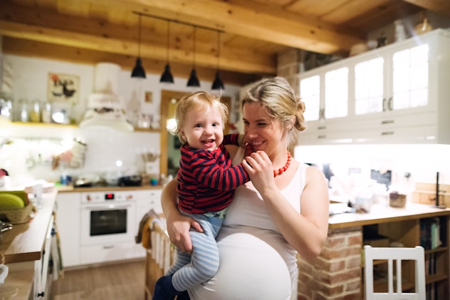 Beautiful pregnant woman carrying a toddler boy in the kitchen at home.