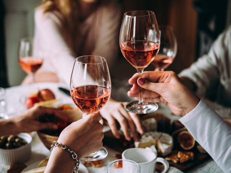 Two girls hold up their glasses of rosé during a Friendsgiving dinner.