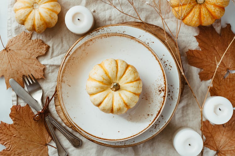 A fall place setting includes white and brown decorated plates, leaves, candles, and pumpkins, makin...