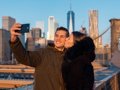 A couple poses for a selfie with NYC skyline in the background.