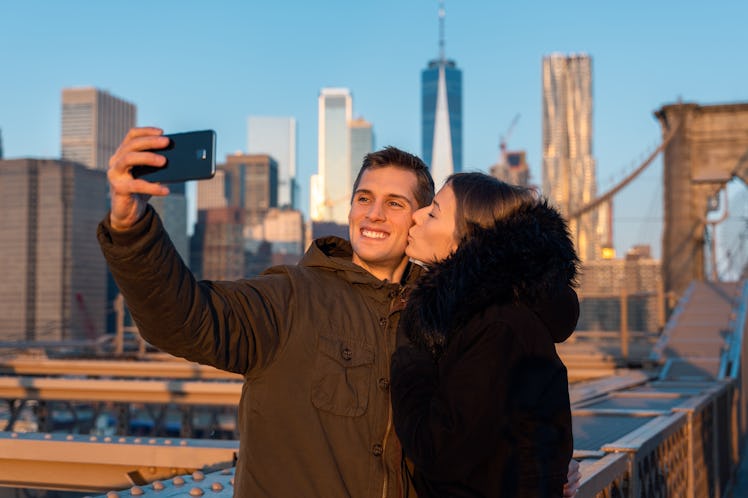 A couple poses for a selfie with NYC skyline in the background.