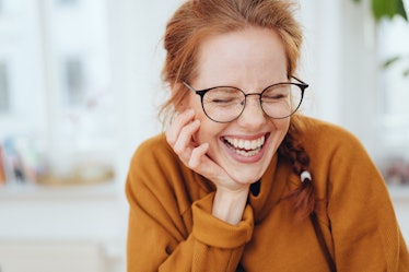 Pretty red-haired girl with pigtail, wearing glasses and orange sweatshirt, laughing with her eyes c...
