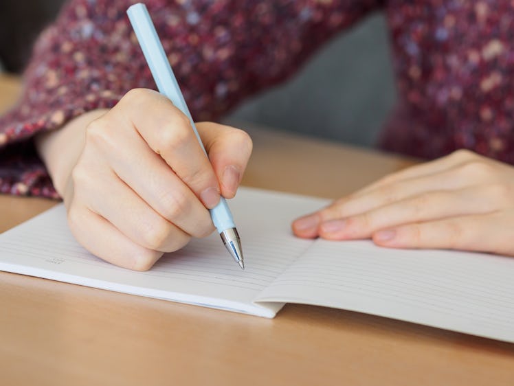 Close up of woman's hands writing in notepad placed on wooden desktop.
