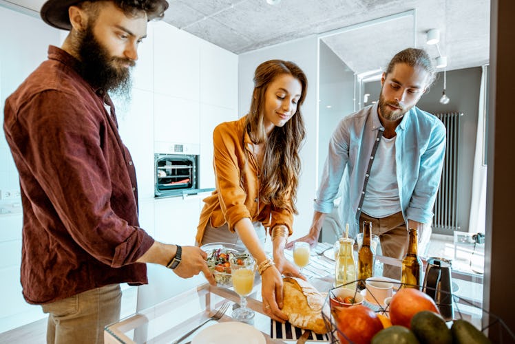 A woman prepares for hosting Friendsgiving in her first apartment by laying food out on a glass tabl...