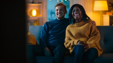 Happy Diverse Young Couple Watching Comedy on TV while Sitting on a Couch, they Laugh and Enjoy Show...