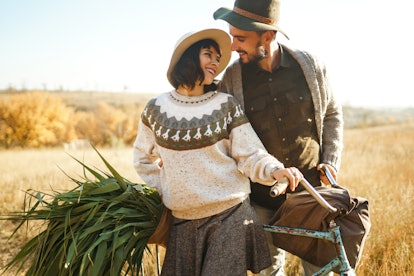 A stylish couple poses with a bicycle and a bag of fresh produce in a field on Thanksgiving.