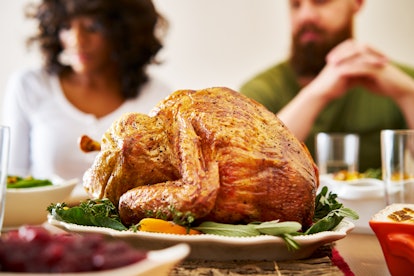 Two people sit behind a turkey platter at a table before they enjoy Thanksgiving dinner.