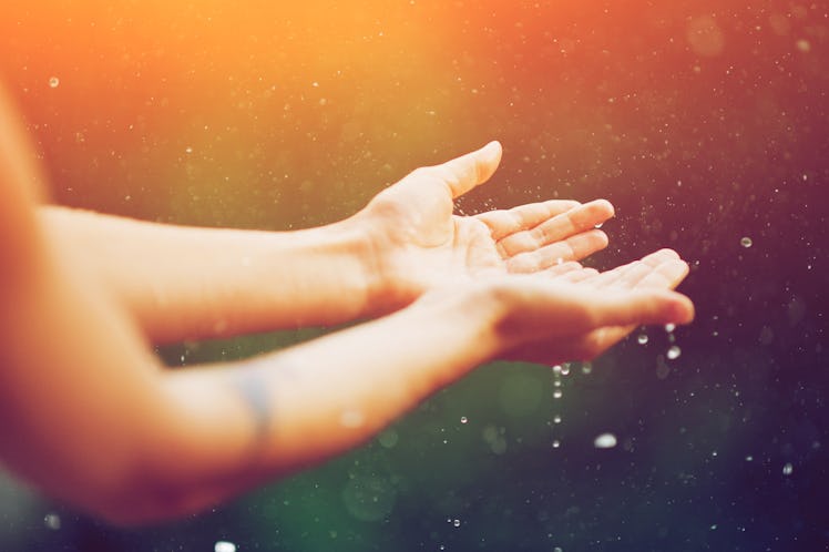 hand catching rain drops on blurred background. Woman hands praying for blessing from god on sunset....