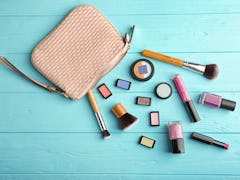 A beige-colored makeup bag on a blue table has cosmetic products and brushes next to it.