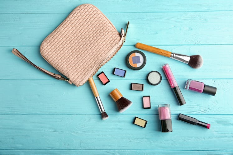 A beige-colored makeup bag on a blue table has cosmetic products and brushes next to it.