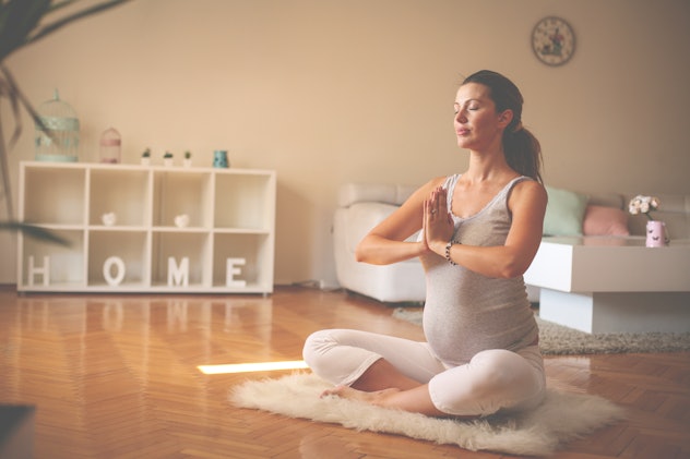 Pregnant woman meditates indoor in yoga pose. Woman enjoying in meditation. 