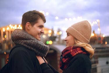 A young couple take a holiday photo together with Christmas lights in the background.