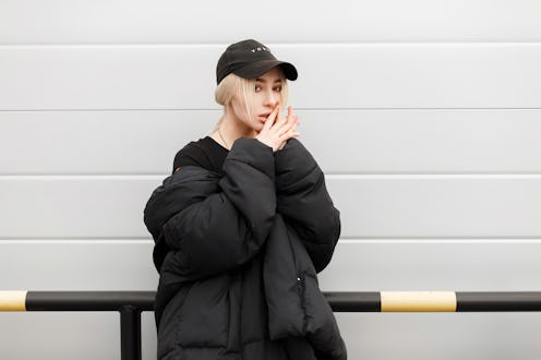 Fashion pretty model girl in fashionable black winter clothes with a cap near a modern metal wall