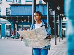 A woman holds a map and her phone outside of a train station in a major city.