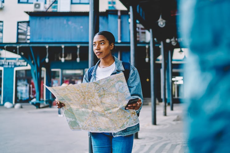 A woman holds a map and her phone outside of a train station in a major city.