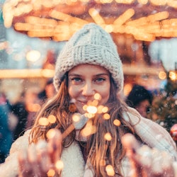 Girl walking in Christmas market decorated with holiday lights in the evening. Feeling happy in big ...