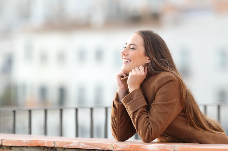 Happy woman heating grabbing jacket in a balcony in winter