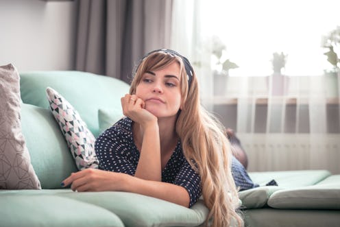 Sad disappointed woman lying on couch and thinking about something at home, casual style indoor shoo...