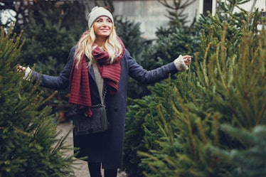 A blonde woman smiles and walks amongst a row of Christmas trees.