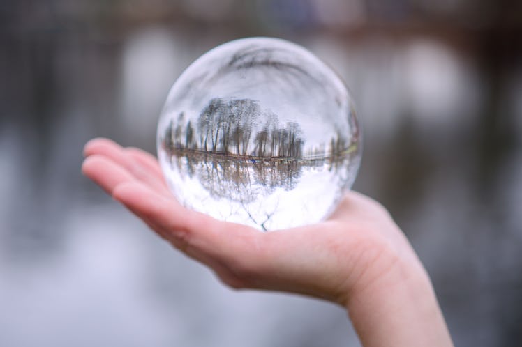 closeup of hand outdoors holding a glass sphere with reflection of trees
