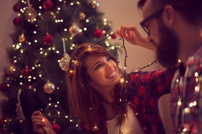 Beautiful young couple in love decorating Christmas tree, arranging the christmas lights and having ...