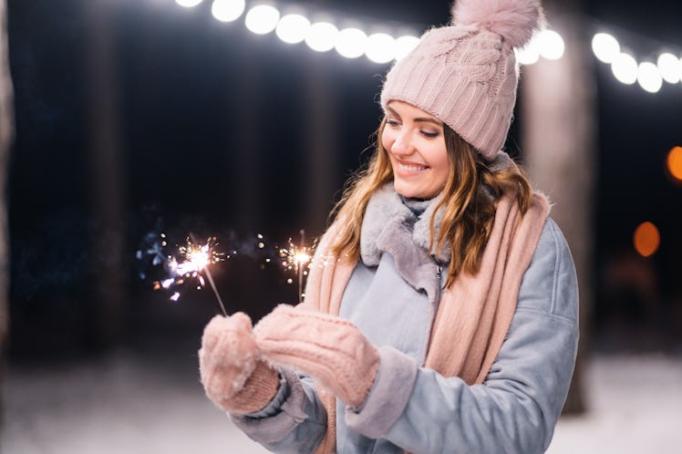 Beautiful girl with sparklers in hands. Happy winter time in the forest. The girl is dressed in a bl...
