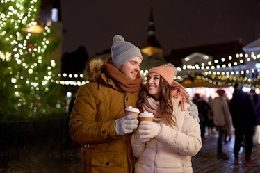 A happy couple drinks coffee outside at a Christmas market.