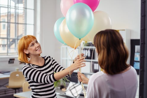 Two female business partners or colleagues holding a bunch of multicolored party balloons with a hap...