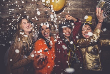 A group of friends laugh and dance under confetti on New Year's Eve.