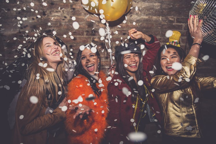 A group of friends laugh and dance under confetti on New Year's Eve.