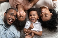 Affectionate african american parents and cute small kids laughing lying on bed together, happy mixe...