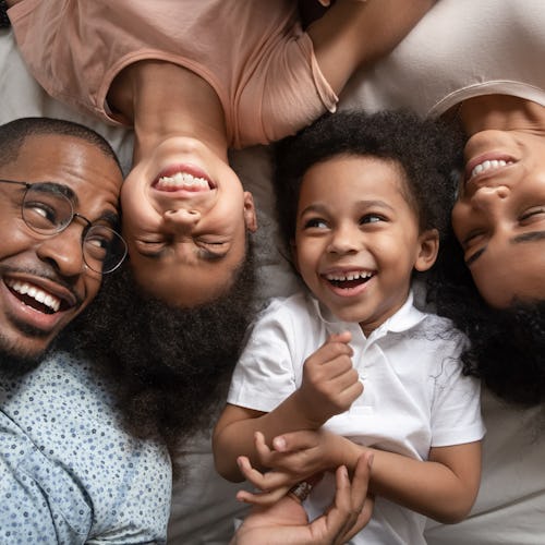 Affectionate african american parents and cute small kids laughing lying on bed together, happy mixe...