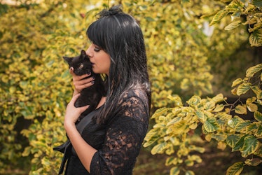 Halloween party concept, mysterious girl with black cat. Beautiful young dark witch woman. Inspirati...
