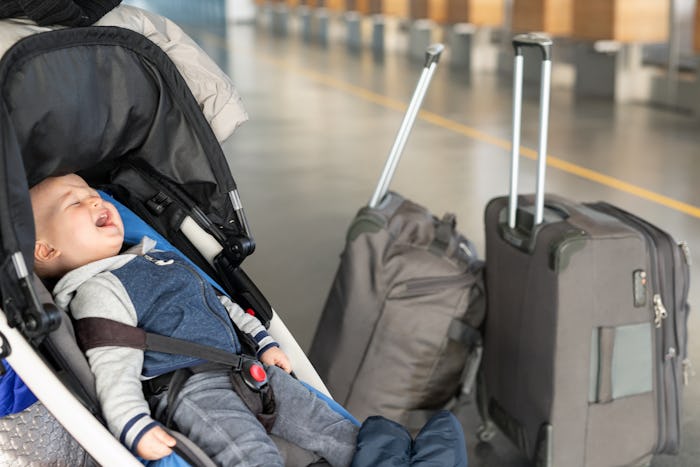 Screaming baby boy sitting in stroller near luggage at airport terminal. Child in carriage near chec...