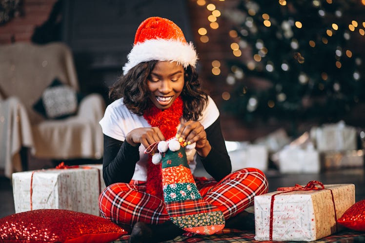 African american woman holding christmas presents by the christmas tree