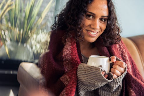 Young hygge woman drinking warm coffee on sofa at home